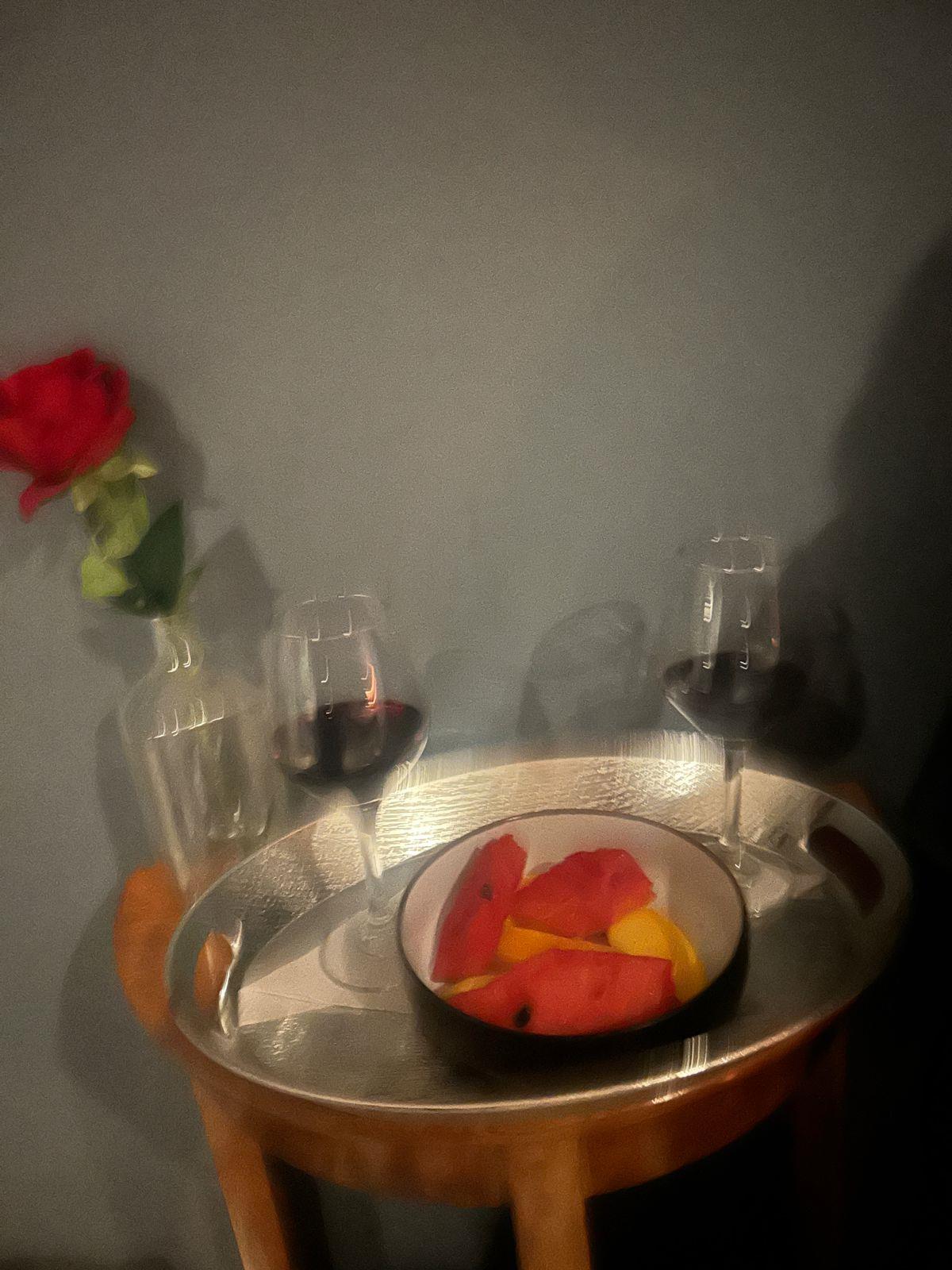 Mesa con copas de vino, fruta y una rosa junto a la camilla